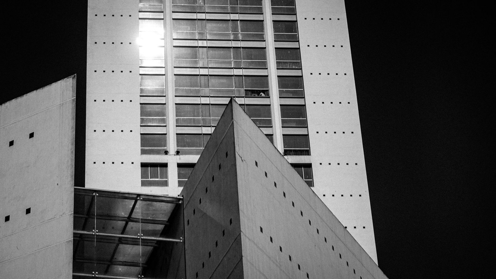 Glass towers cut the sky / into geometric puzzles. / A homeless man lies /...